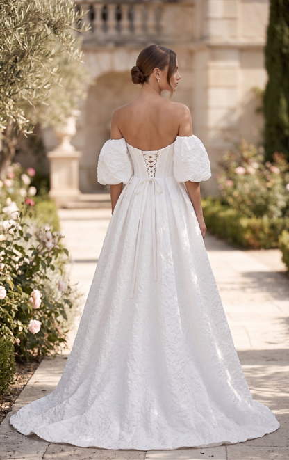 Woman in a white lace wedding dress standing in a garden setting.