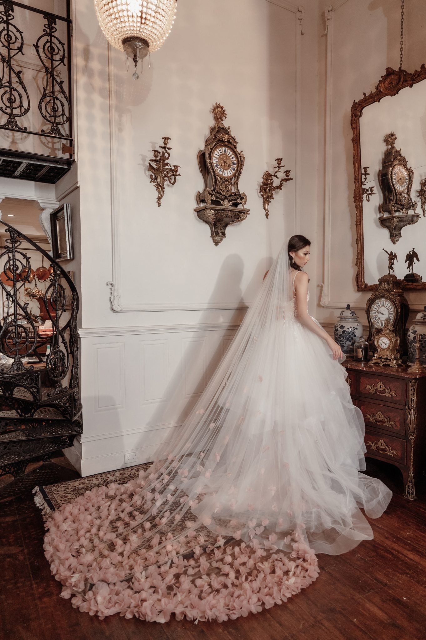 Woman in a wedding dress with a long train in an elegant room with decorative clocks and furniture.