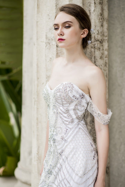 Woman in an elegant off-shoulder dress standing against a textured wall.