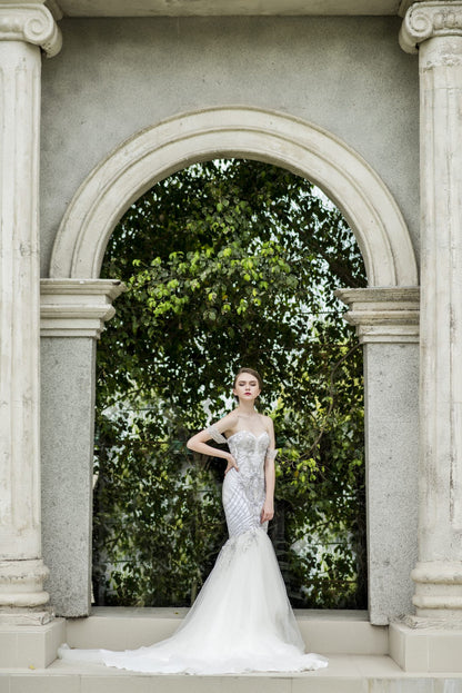 Woman in a white wedding dress standing in front of an archway with greenery.