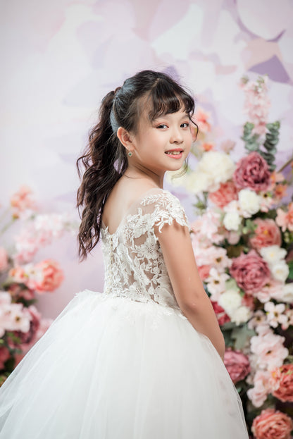 Young girl in a white dress standing in front of a floral backdrop