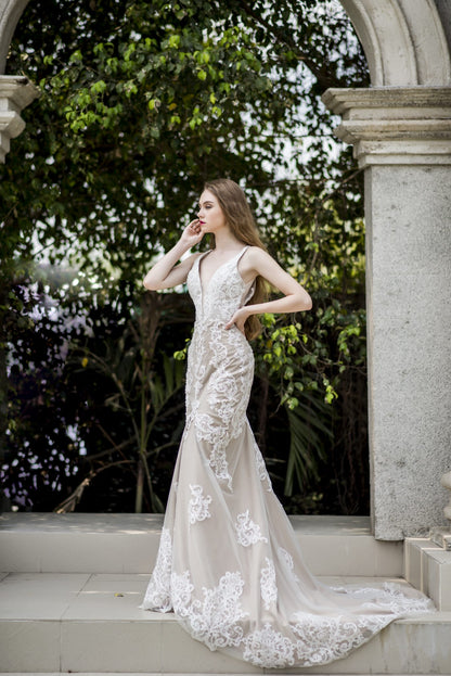Woman in a white lace wedding dress standing outdoors with greenery in the background