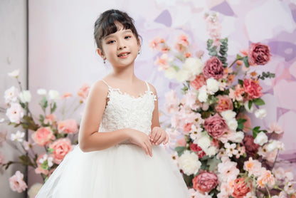 Young girl in a white dress standing in front of a floral arrangement