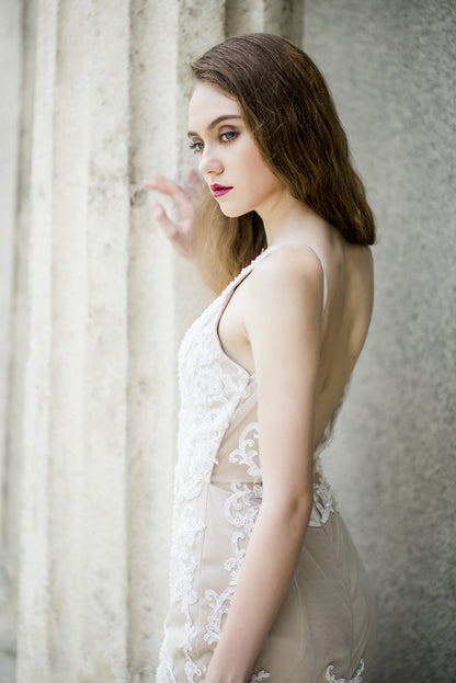 Woman in a white lace dress standing against a textured wall.