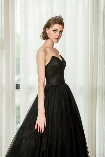 Woman wearing a black strapless gown in front of white curtains