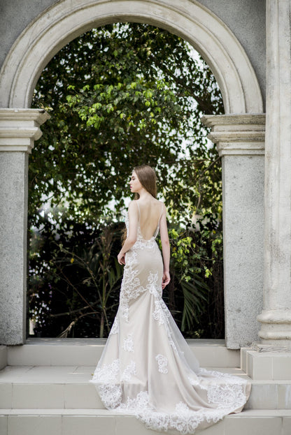 Woman in a white wedding dress standing in front of a stone archway with greenery.