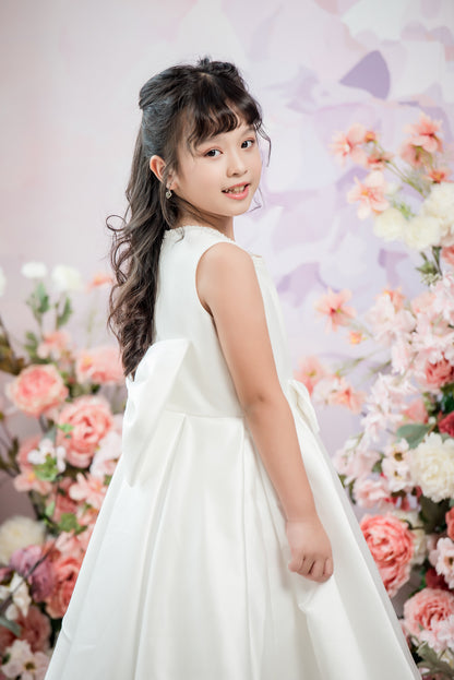 Young girl in a white dress standing in front of a floral backdrop