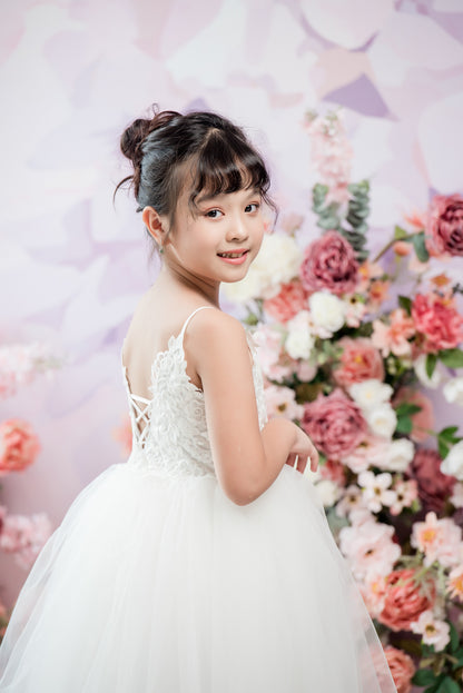 Young girl in a white dress standing in front of a floral backdrop