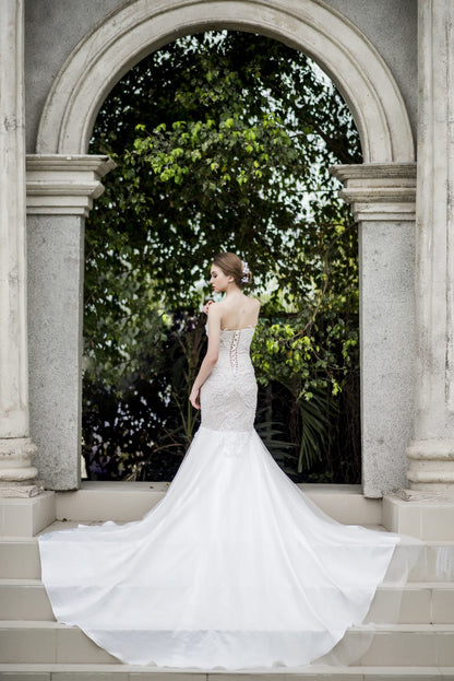 Woman in a white wedding dress standing in front of an archway with greenery.
