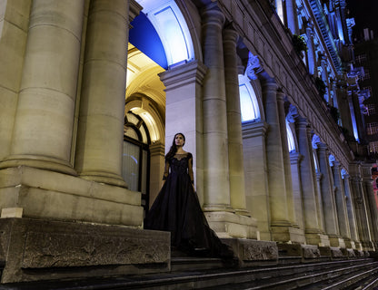 Woman in a black dress standing in front of a grand building with columns at night.