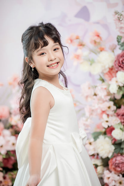 Young girl in a white dress standing in front of a floral backdrop