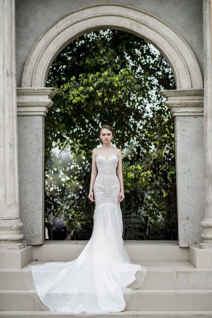 Woman in a white wedding dress standing in front of an archway with greenery.